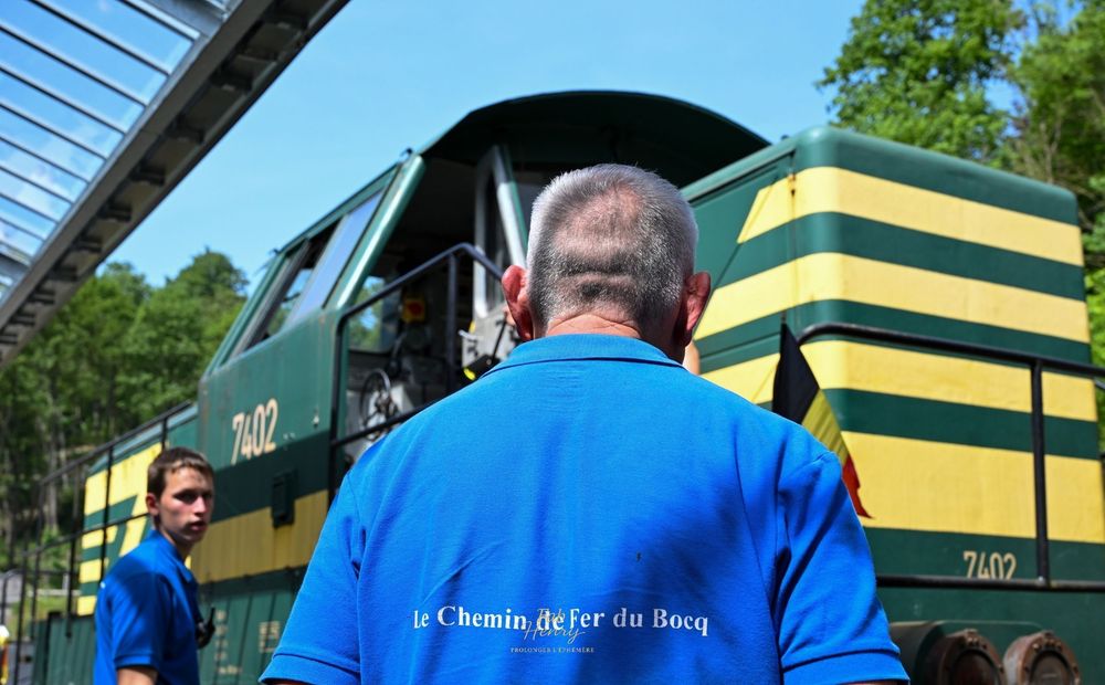 Locomotive verte et jaune, personnage en chemise bleue au premier plan