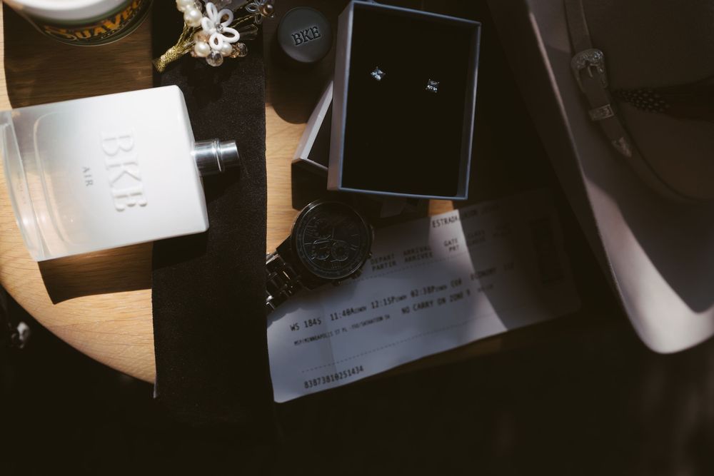 Flat lay of groom accessories including a flask, watch, cufflinks, and a handwritten note.