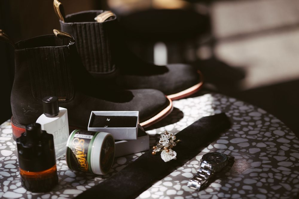 Black boots and grooming products arranged on a marble surface in dramatic lighting.
