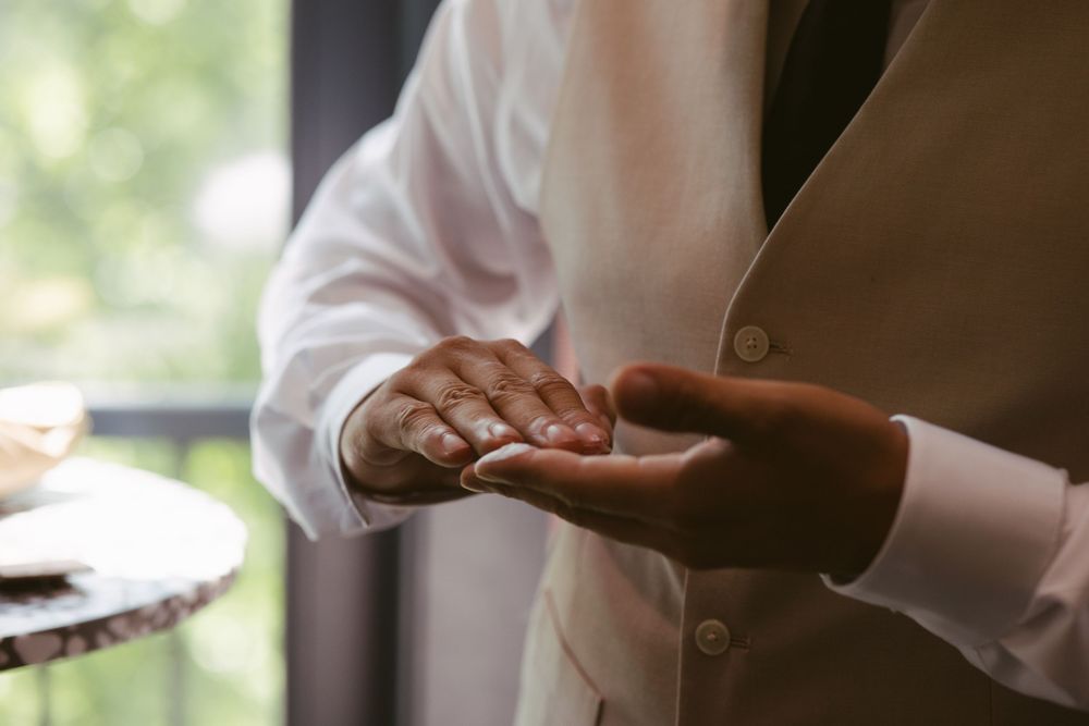 Groom in white shirt and vest holding a wedding ring in his palm during wedding preparation.