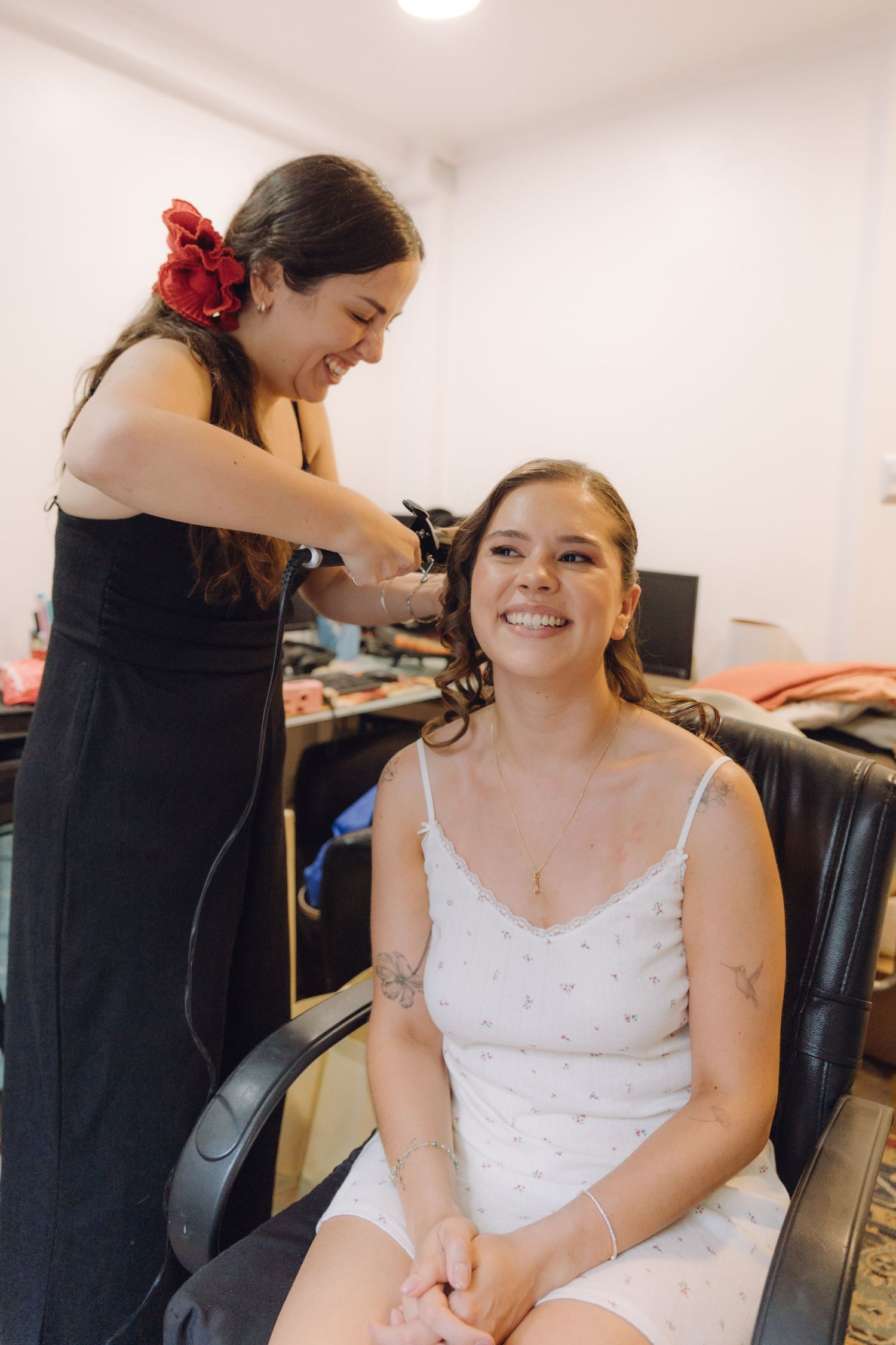 A happy bride smiles while a hairstylist curls her hair in preparation for her wedding day.