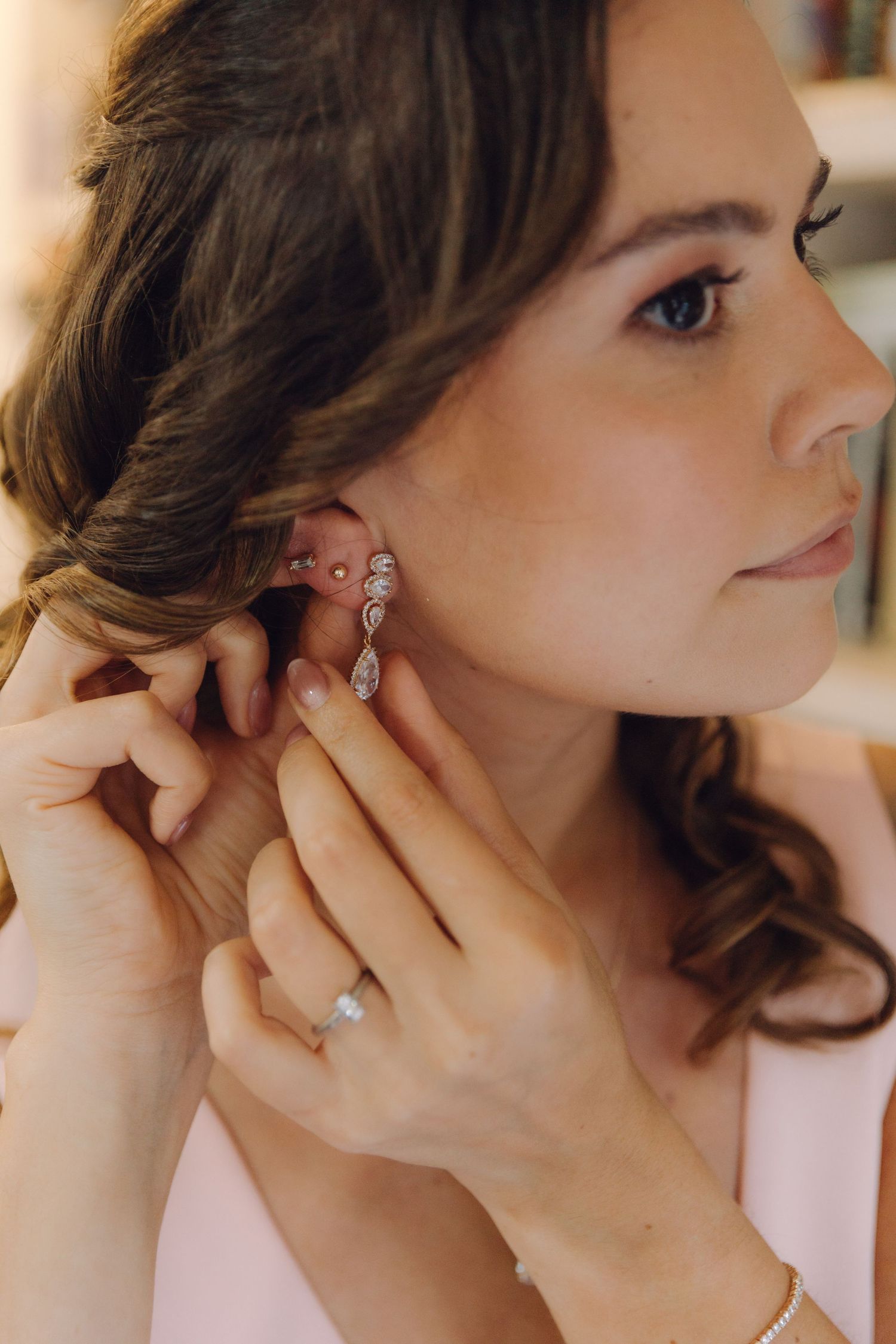 Close-up of bride putting on sparkling crystal drop earring with engagement ring visible on finger.
