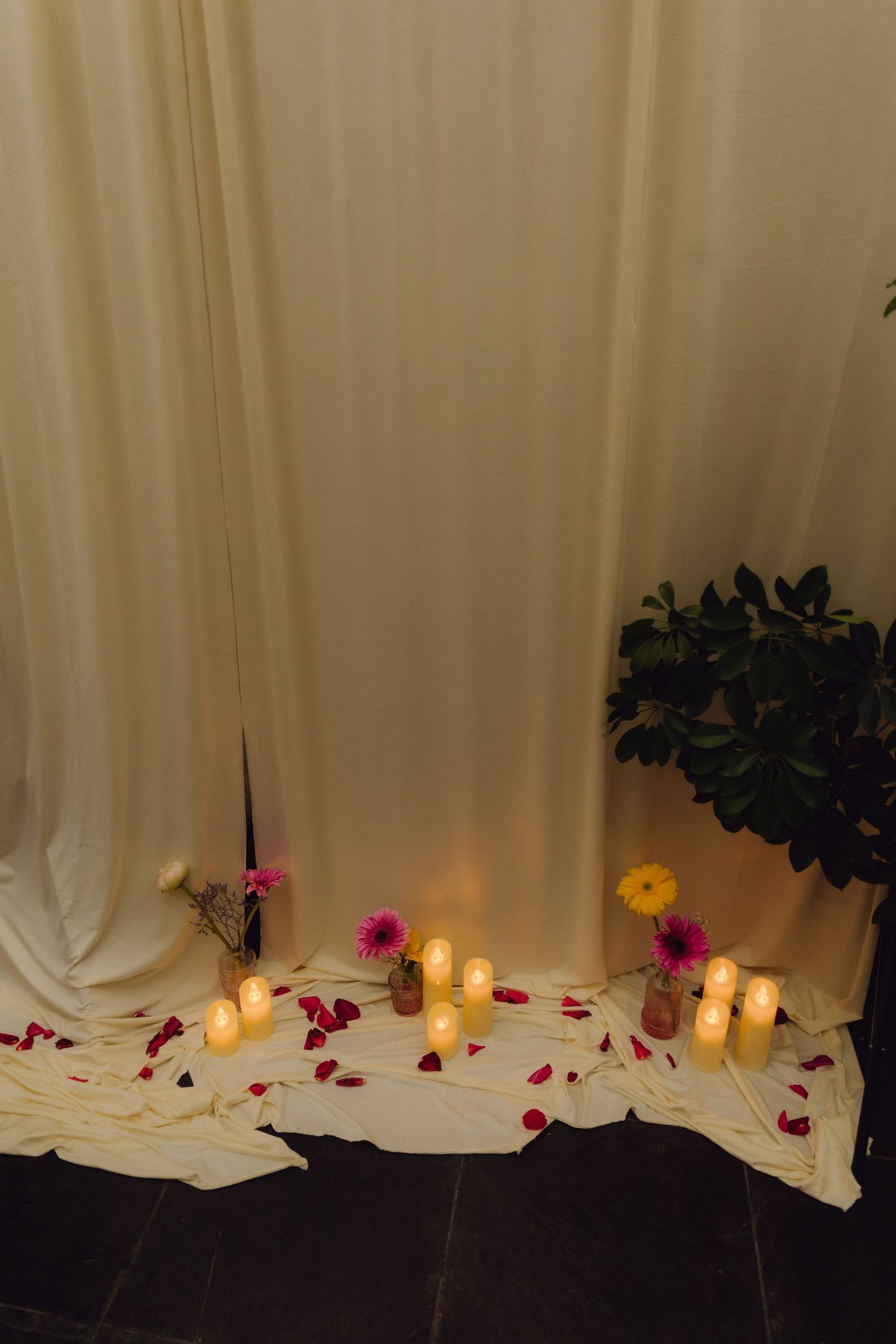 Romantic wedding altar with cream drapes, glowing candles, rose petals and small colorful flowers.