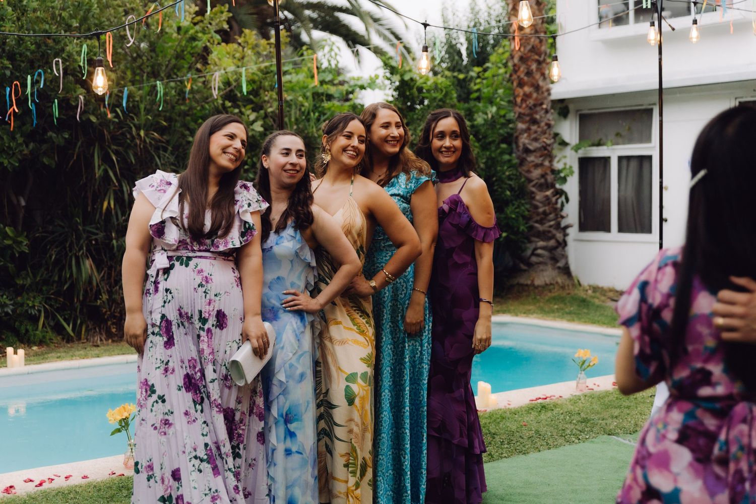 Group of five women in colorful floral formal dresses posing together at an outdoor wedding venue.
