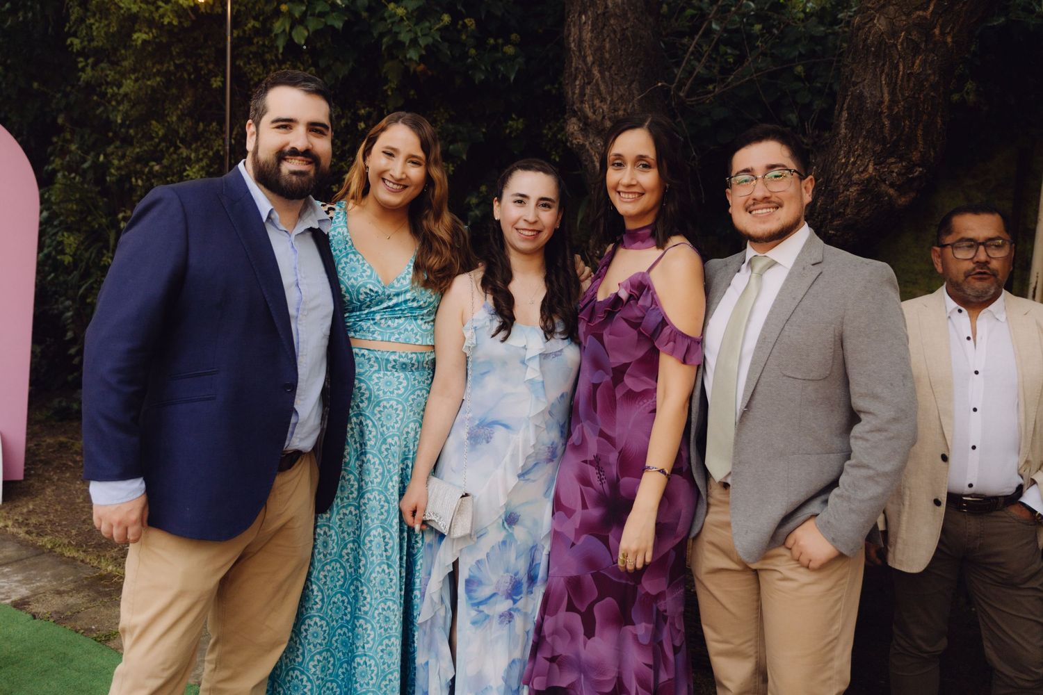 Group of five young adults posing together outdoors at a festive celebration wearing colorful formal attire.