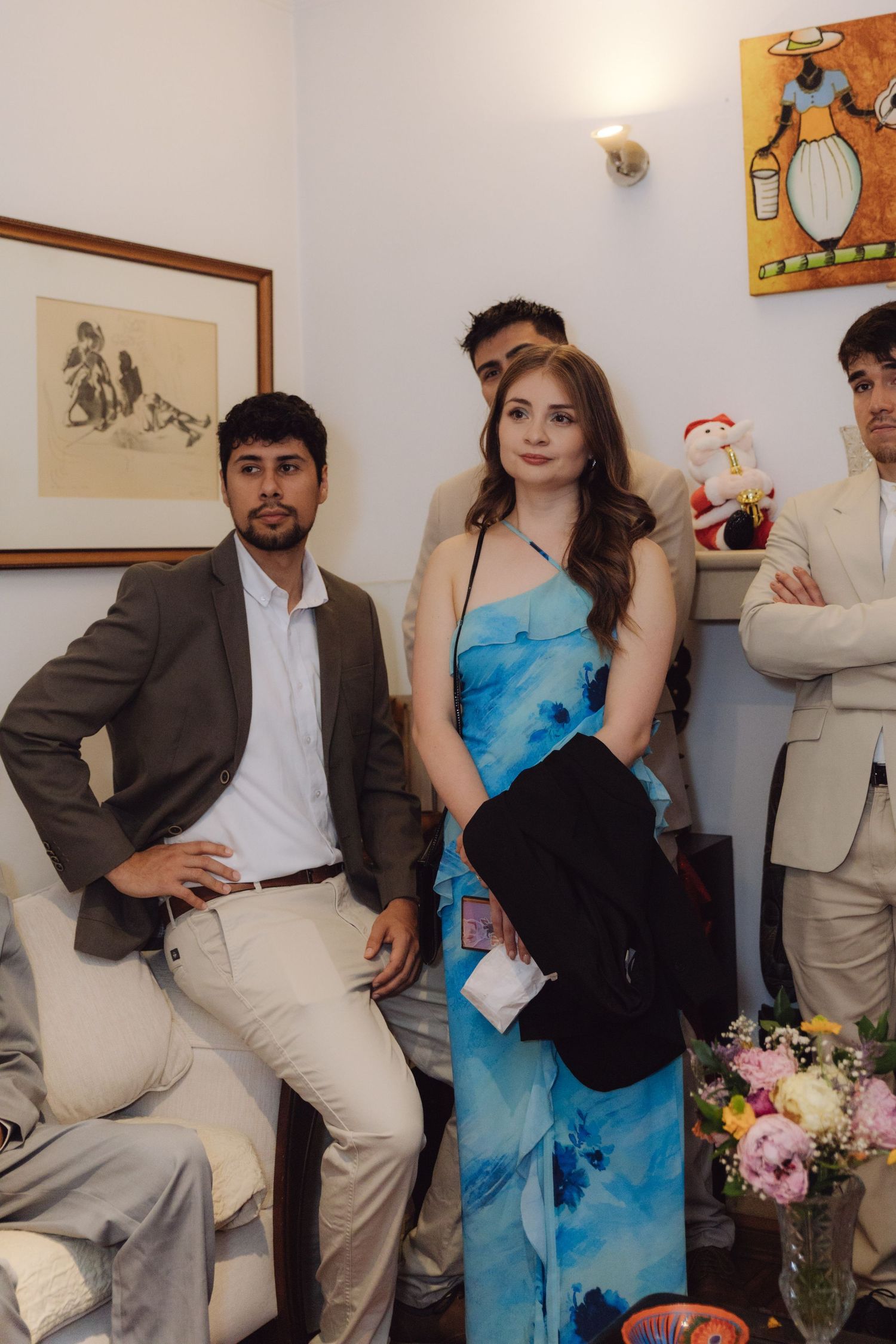 Wedding guests posing indoors including woman in blue floral dress with decorative artwork on walls.
