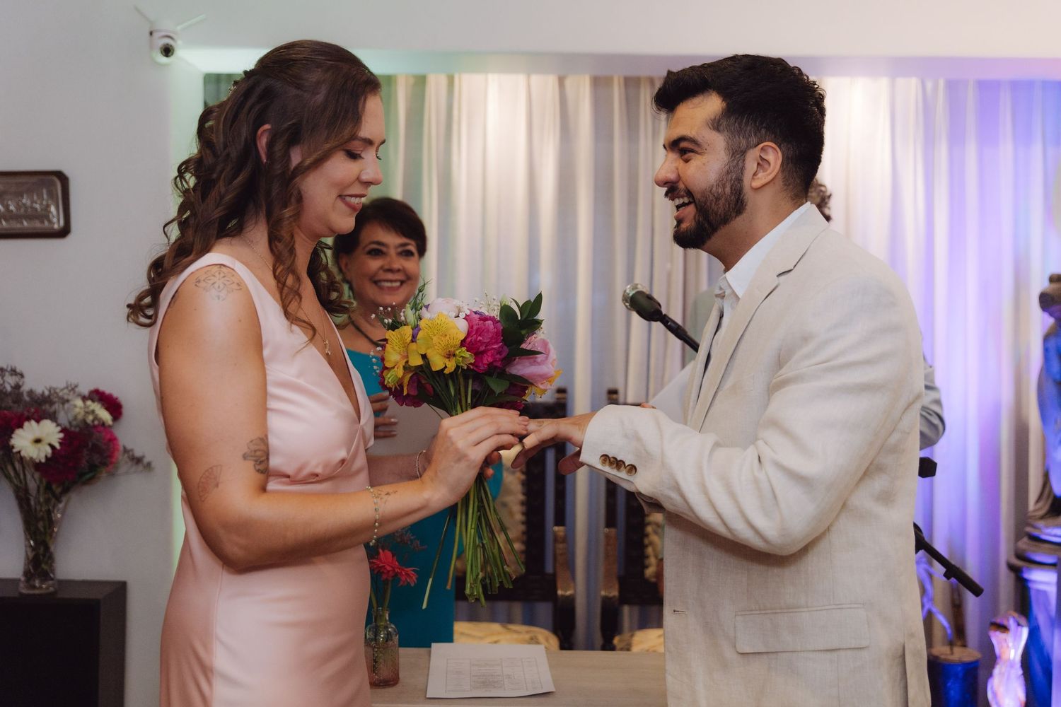 Groom places wedding ring on brides finger during joyful indoor wedding ceremony.