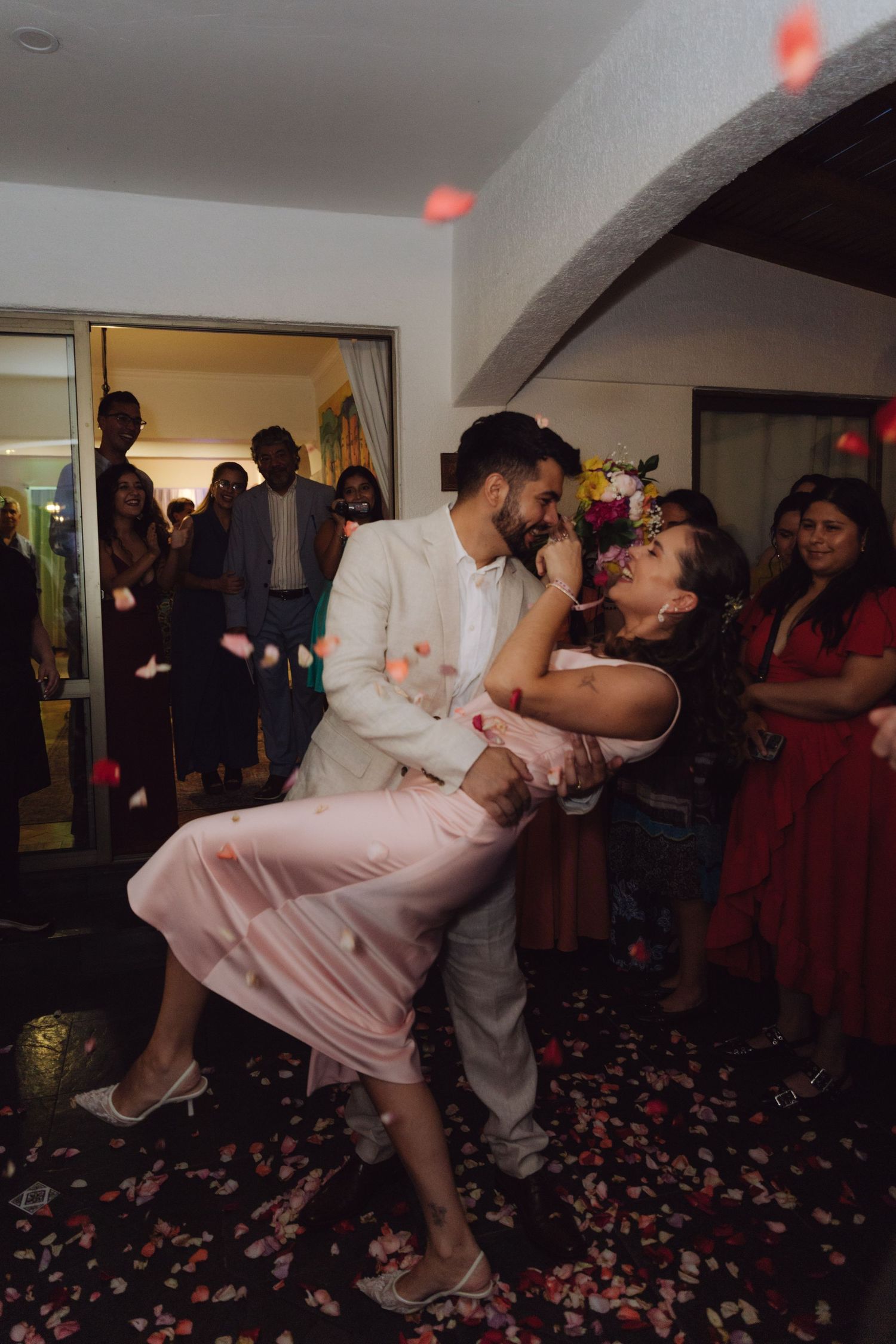 Groom dips bride for romantic kiss as guests celebrate with confetti at wedding reception.