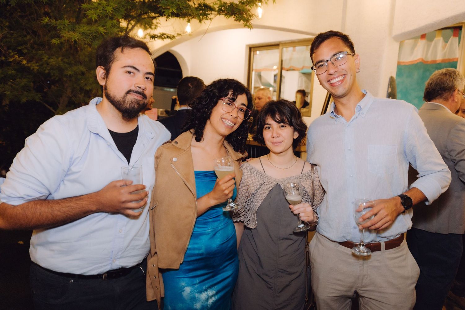 Group of four people posing with wine glasses at an elegant indoor evening social gathering.