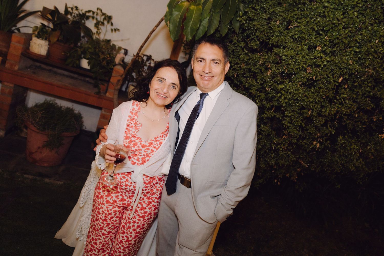 Smiling couple posing together outdoors at night, woman in floral dress and man in light gray suit.