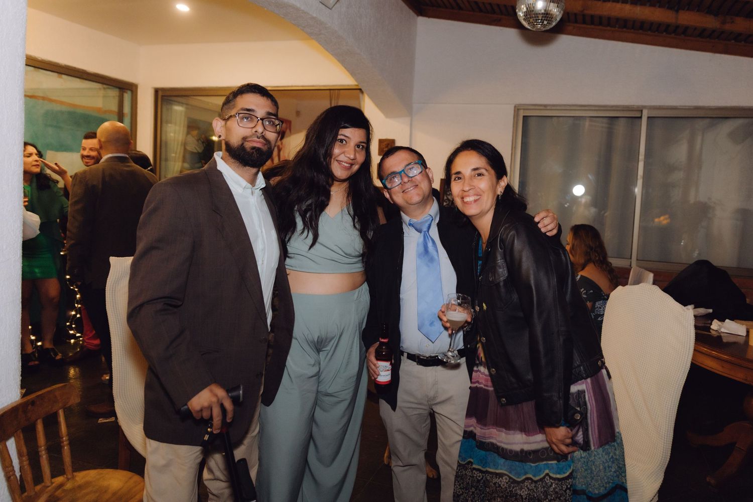Group of four guests smiling together at an indoor evening celebration with holiday decorations.