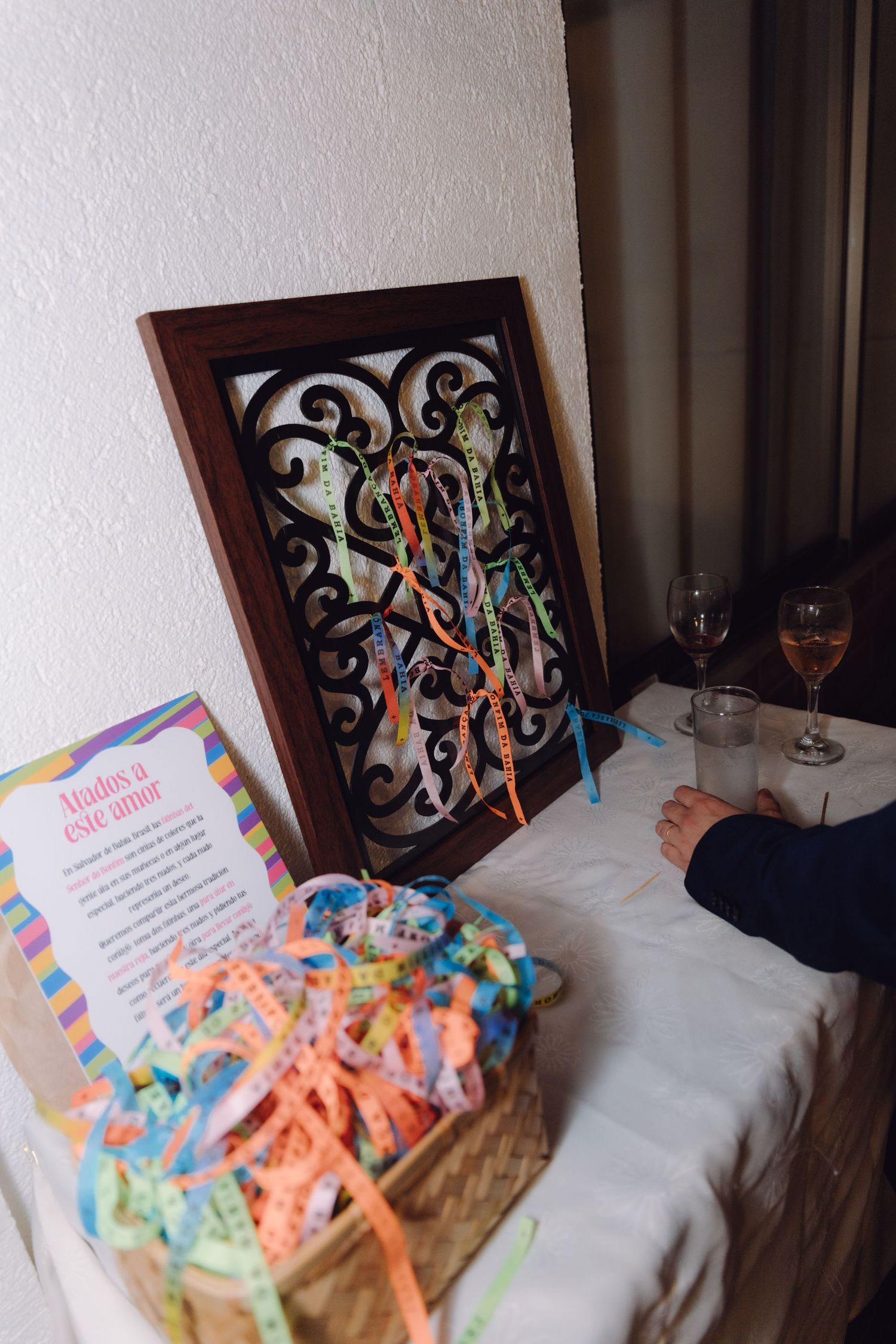 Colorful ribbon bracelets in a basket displayed on a table with decorative framed art at an event.
