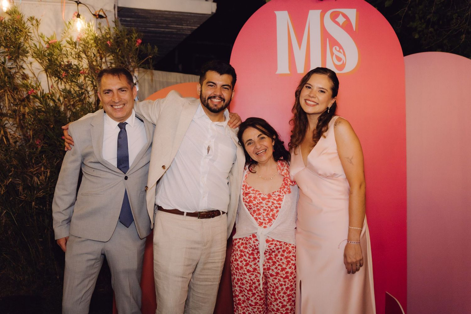 Four people including two men and two women smile together at a pink MS monogram event backdrop.