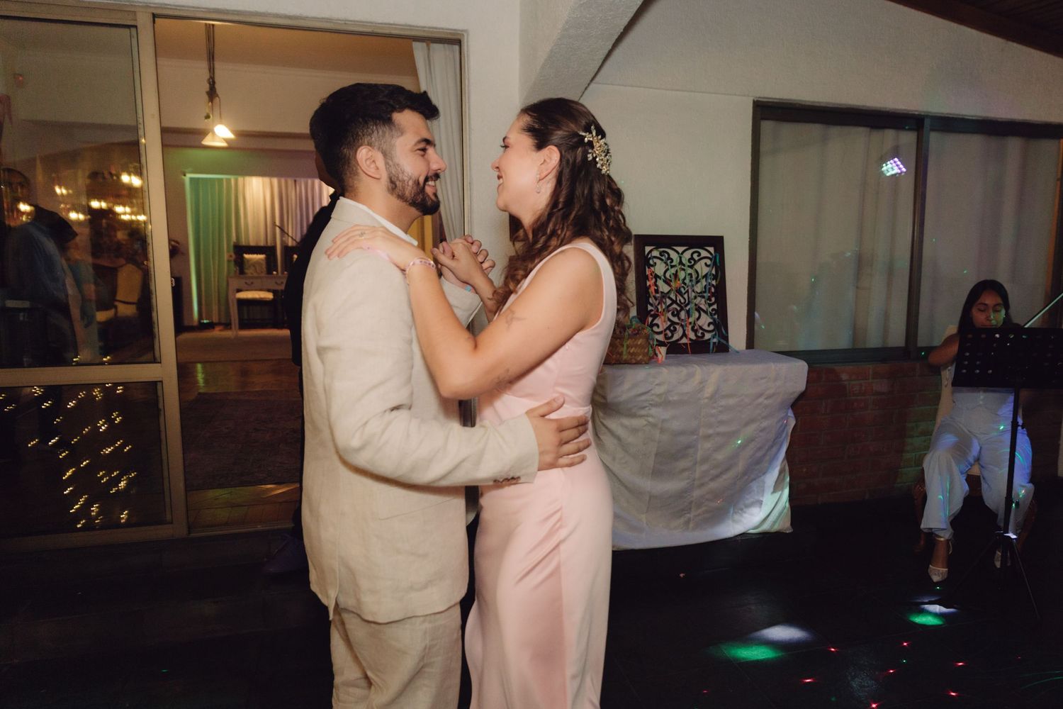 Couple in wedding attire share a romantic dance on a dance floor with colorful lighting.