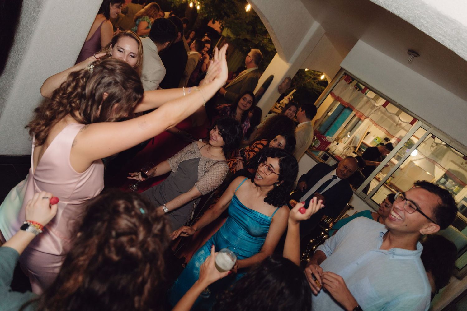 Wedding guests laugh and dance energetically together at a lively indoor wedding reception party.