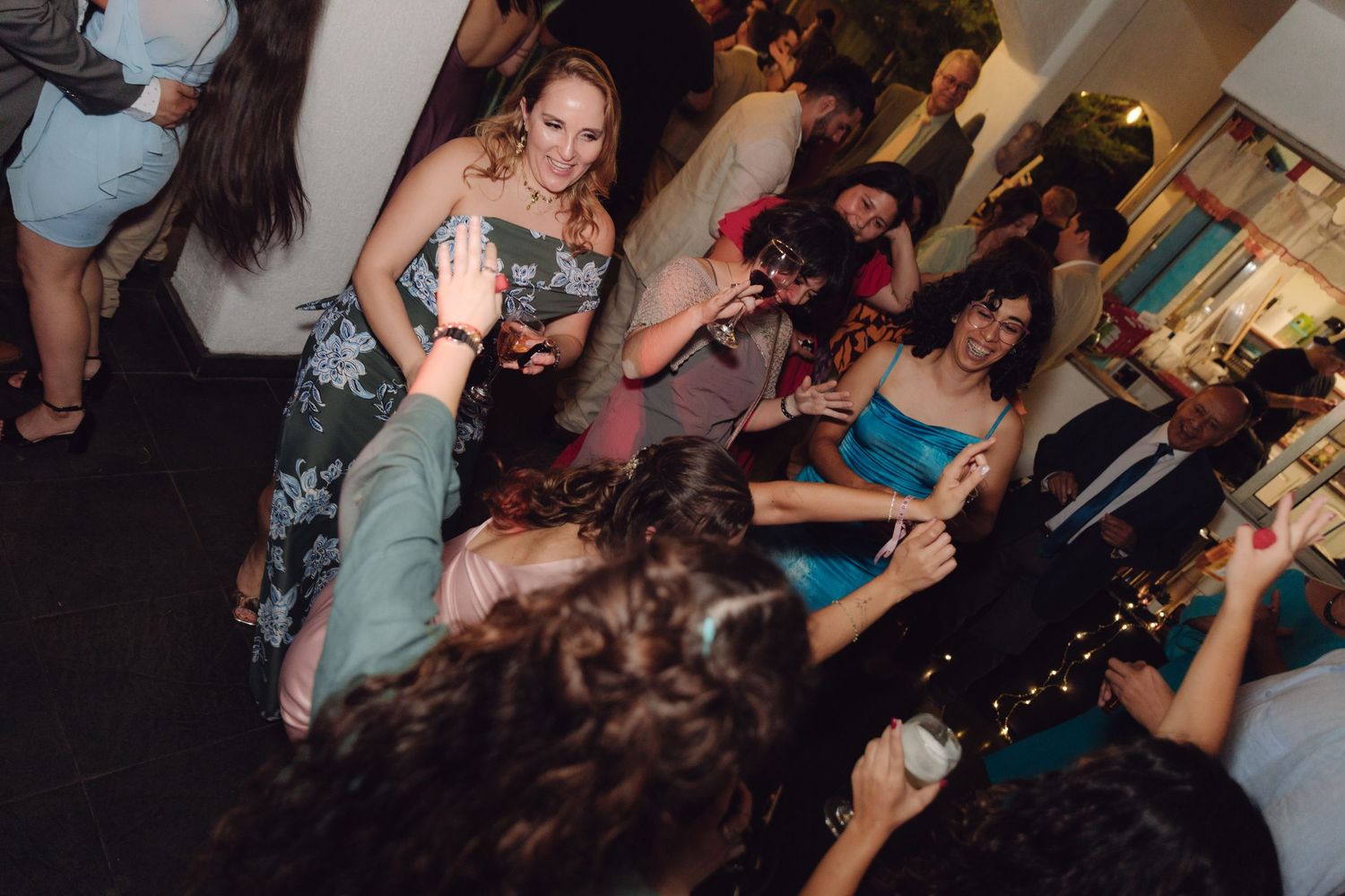 Guests enjoy a lively wedding reception dance floor, with a woman in a floral dress dancing among the crowd.
