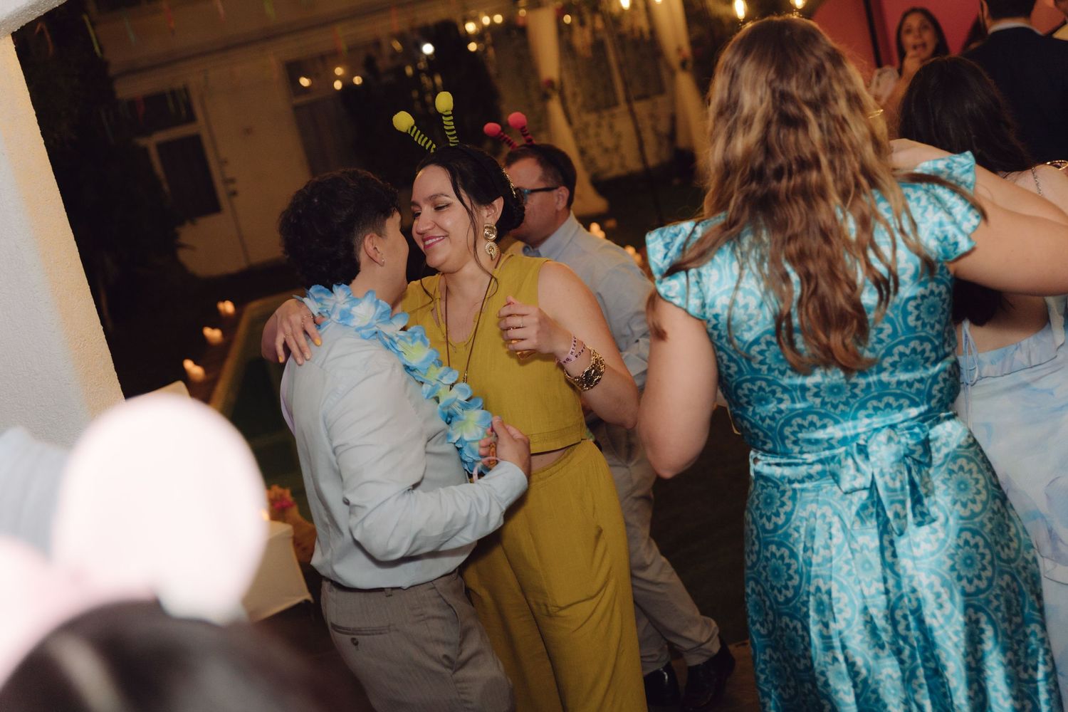Guests dance and socialize at a colorful wedding reception, with a woman in a yellow dress sharing a warm embrace.