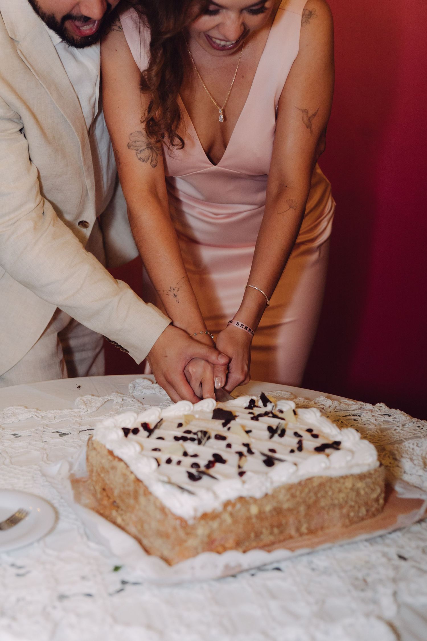 Close-up of bride and groom hands cutting white frosted wedding cake with chocolate decorations.