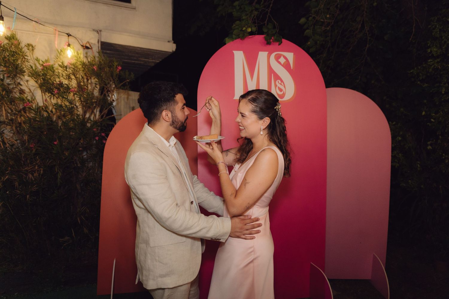 Bride and groom sharing a tender moment in front of pink MS monogram wedding backdrop at night.