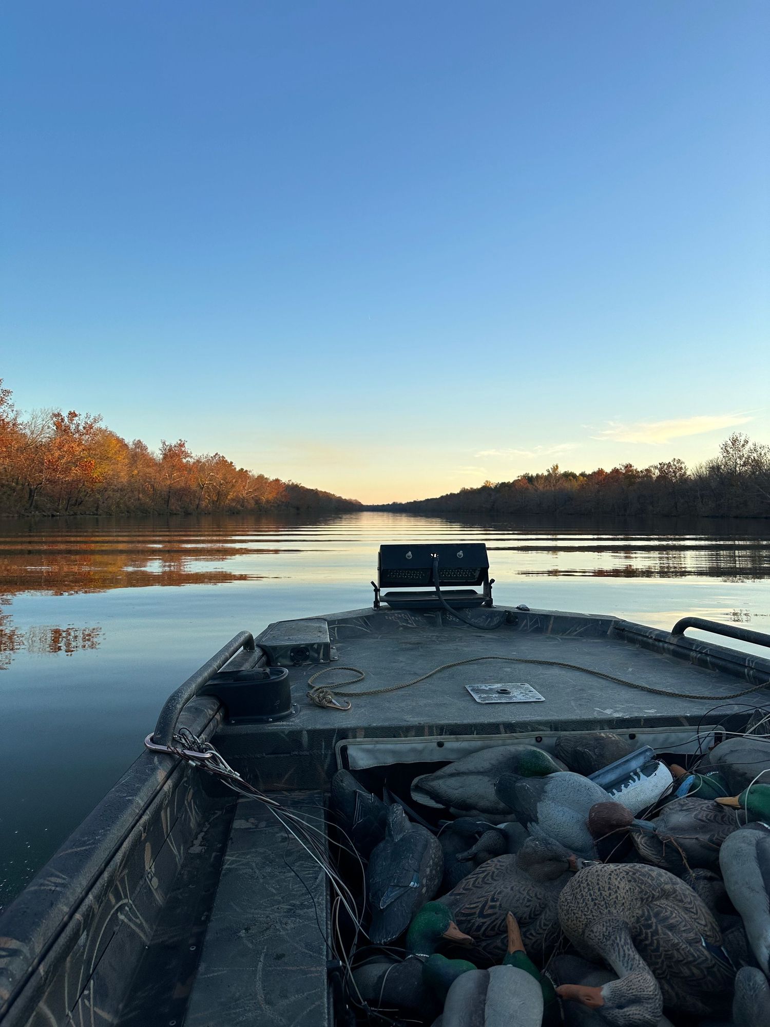 A boat speeding through a calm river at sunset, with water splashing and vibrant orange skies reflecting on the surface.