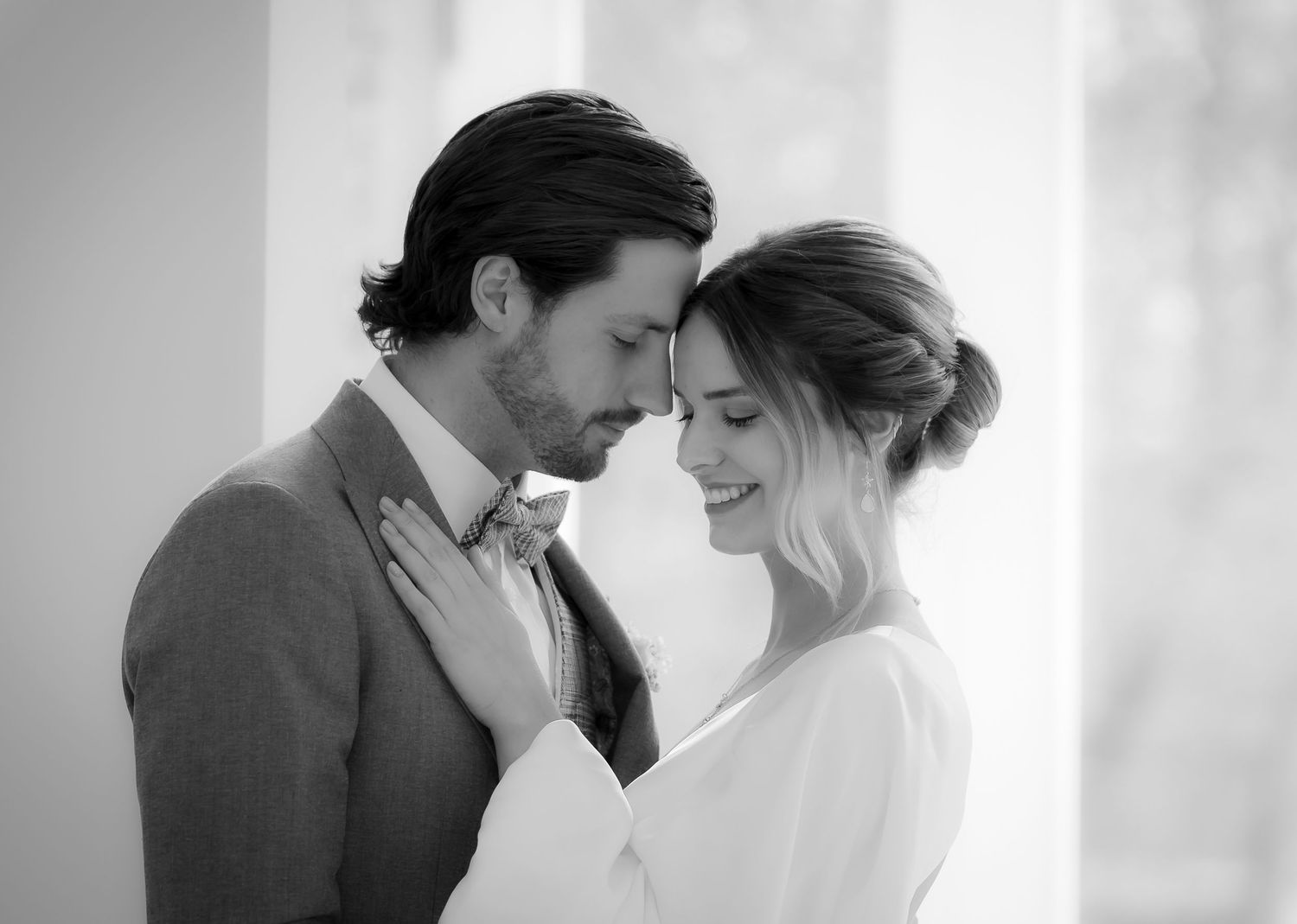 Black and white photo of an elegant couple sharing a romantic moment, touching foreheads in a tender embrace.