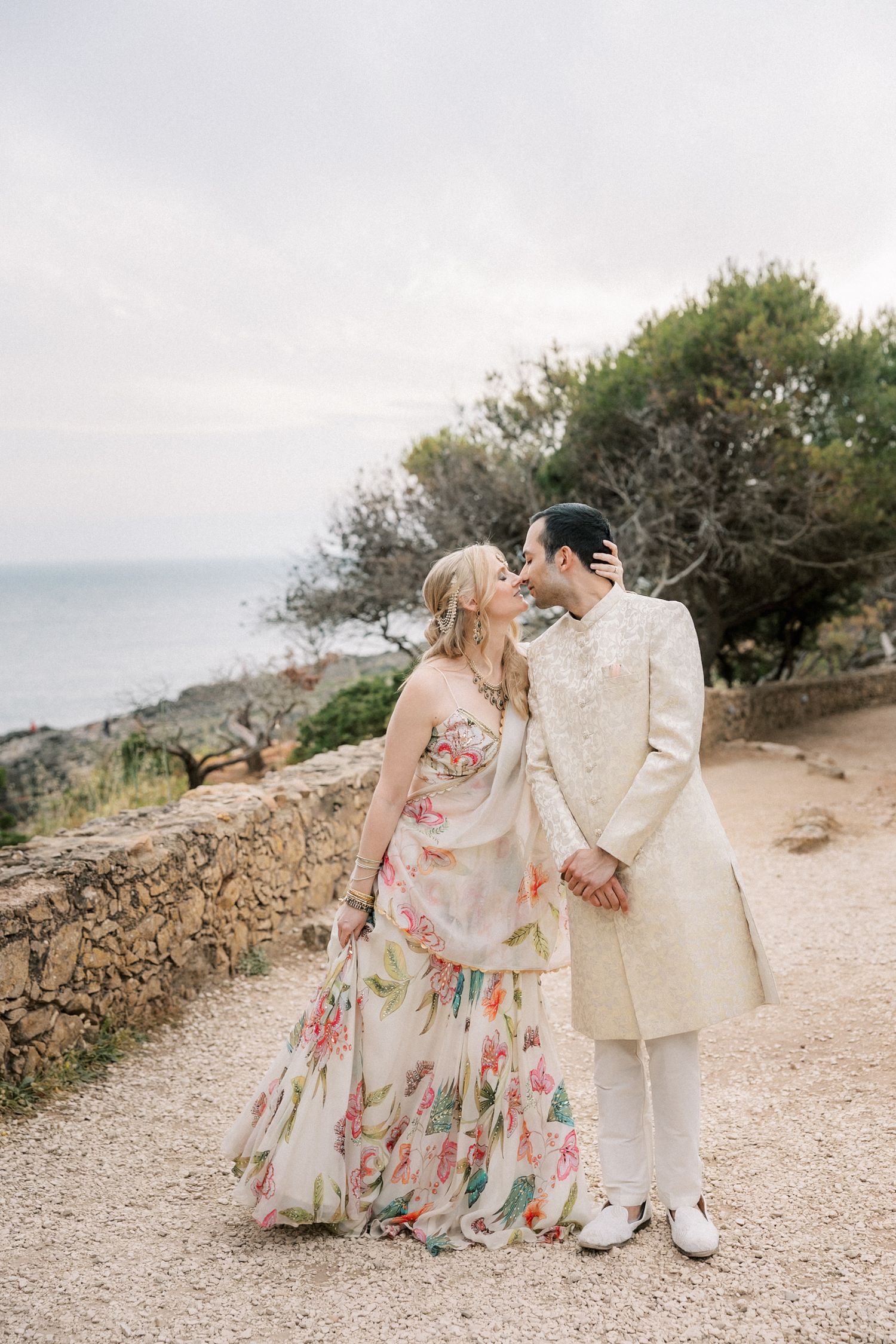 Bride and groom sharing a kiss during their Mehndi celebration overlooking the Atlantic Ocean in Cascais, Portugal.