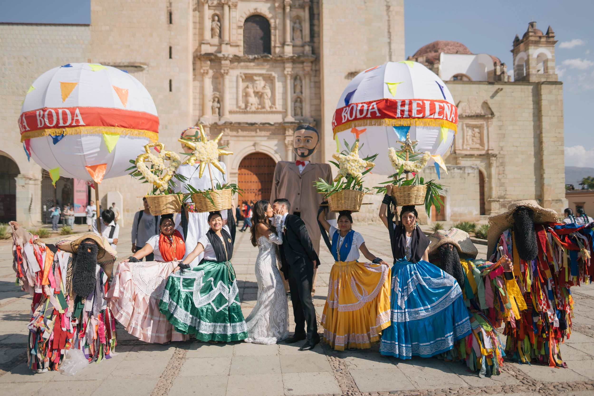 Traditional Mexican wedding celebration outside a historic church in Oaxaca with dancers in colorful dresses and decorative balloons.