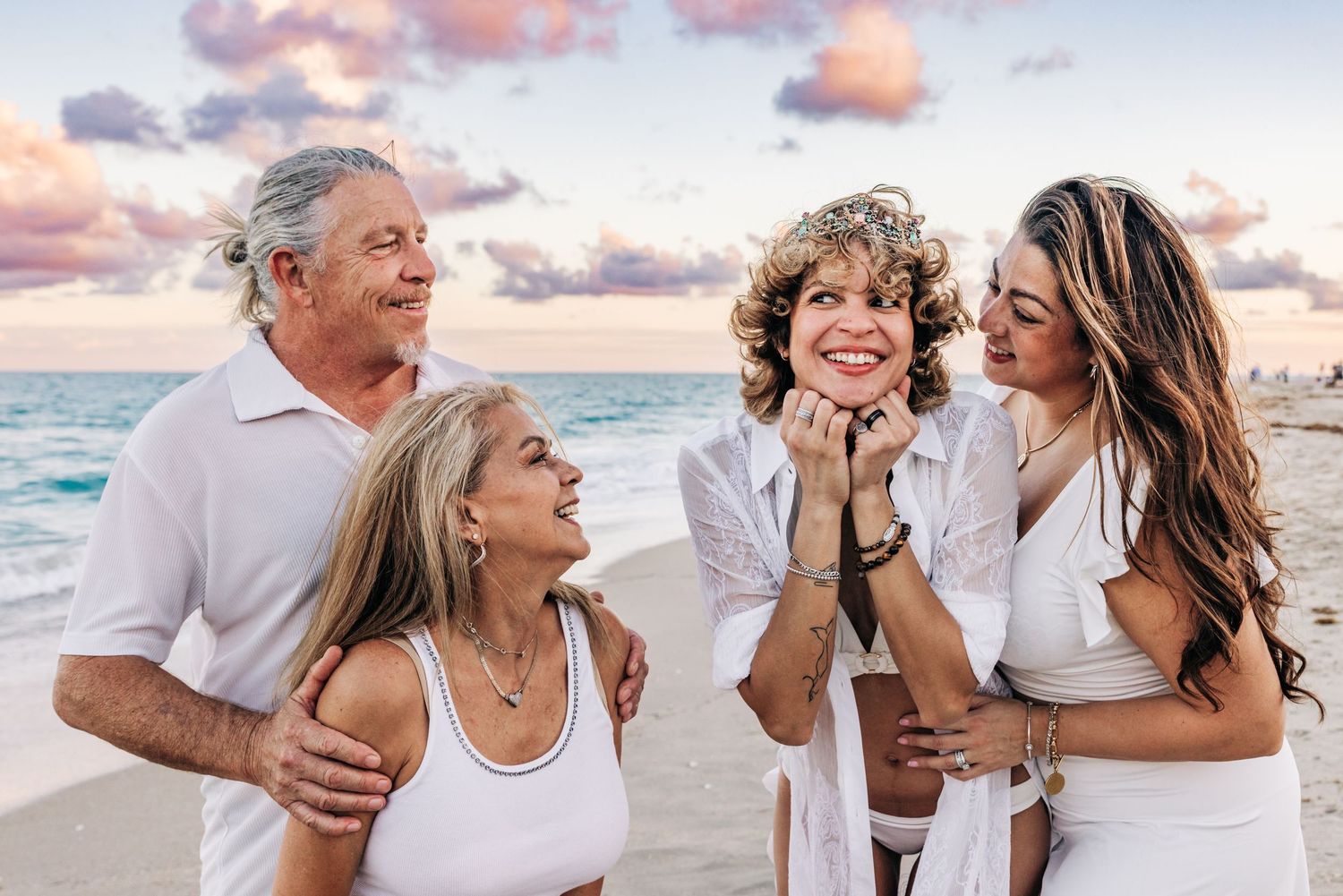 Family of four posing on palm beach at sunset, holding a framed giraffe artwork, wearing white outfits on beach on palm beach.