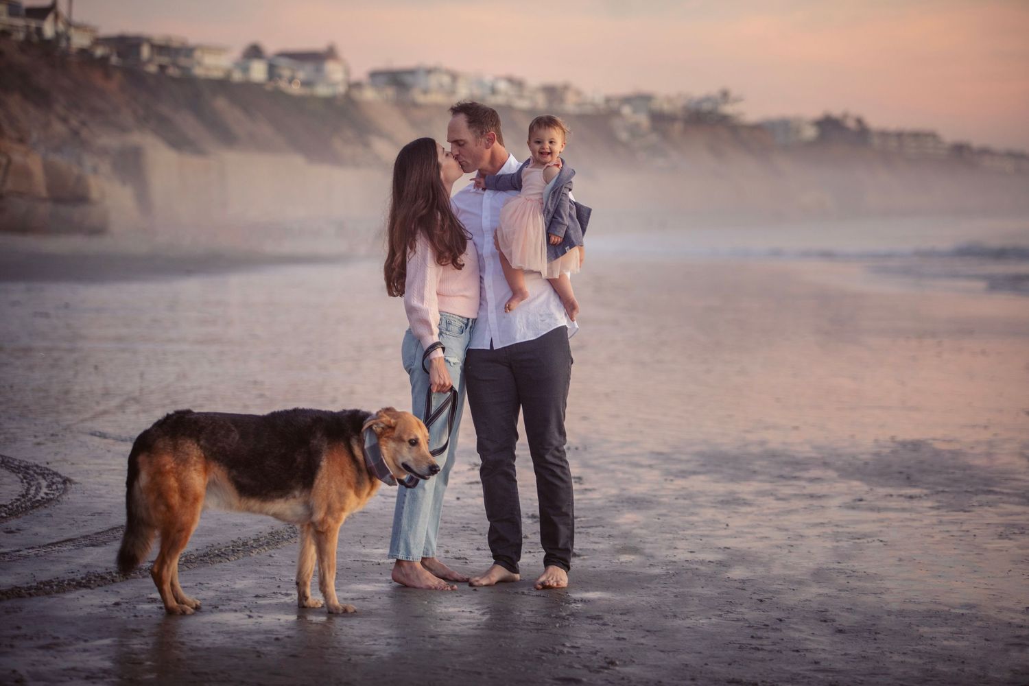 Family of four posing on coastal overlook with ocean views and lush greenery in the foreground.