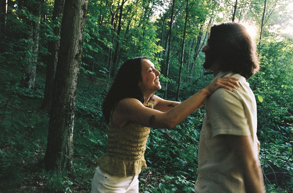 A couple shares a romantic moment dancing together in a lush green forest setting.