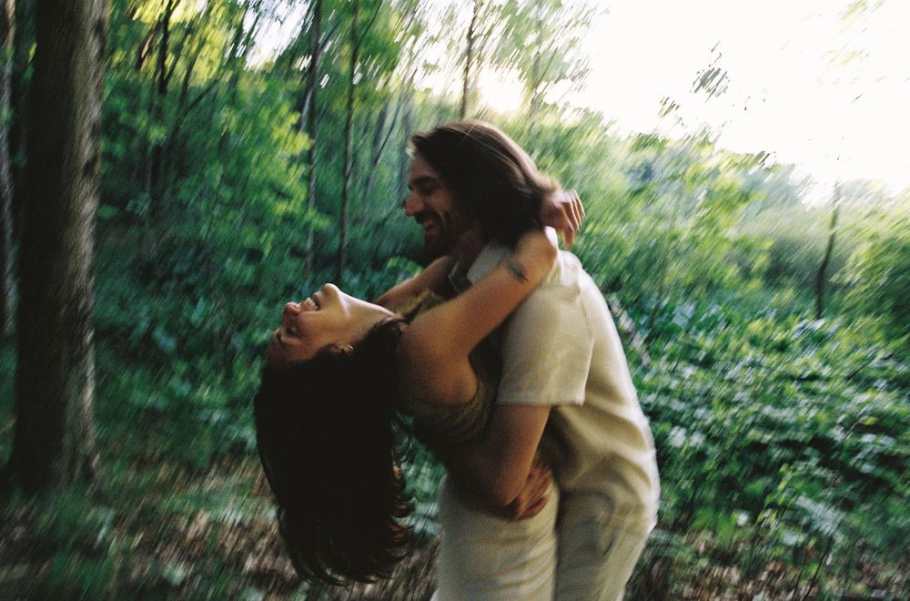Couple embracing and laughing joyfully in a lush green forest setting.