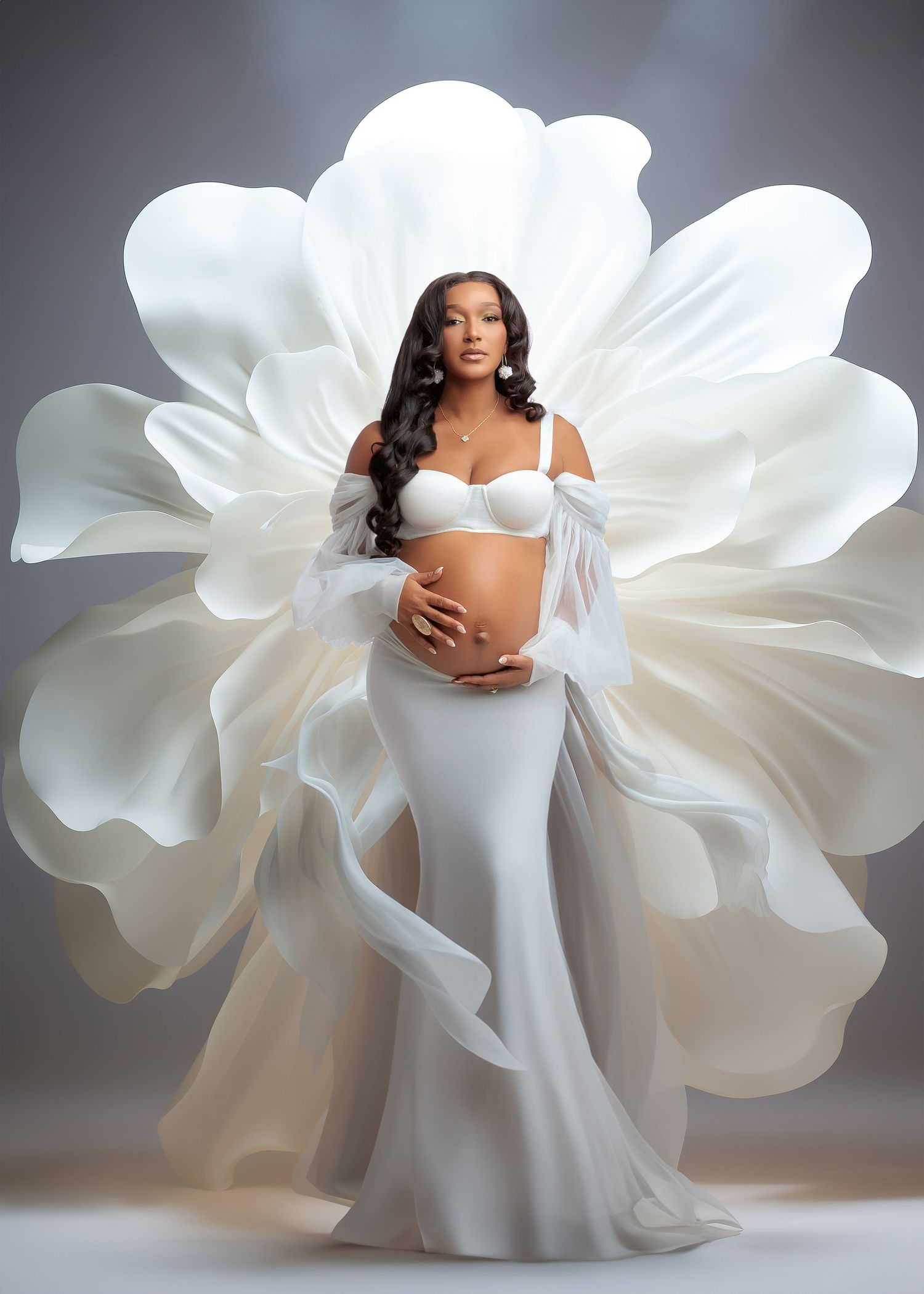 Pregnant woman in white mermaid gown with large floral fabric backdrop, cradling baby bump in elegant maternity photo shoot.