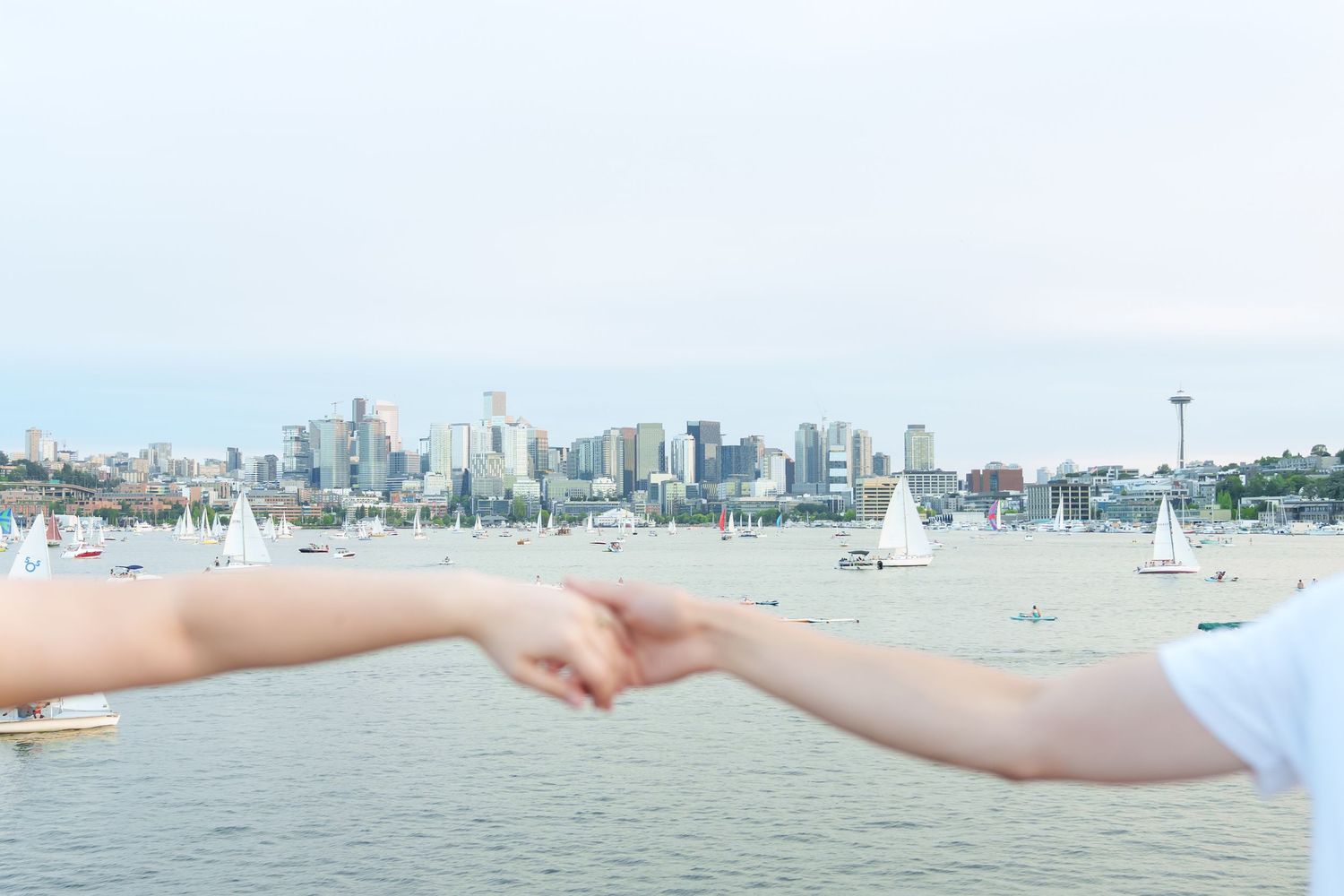 Two people holding hands with Seattle skyline and sailboats on Lake Union in the background.
