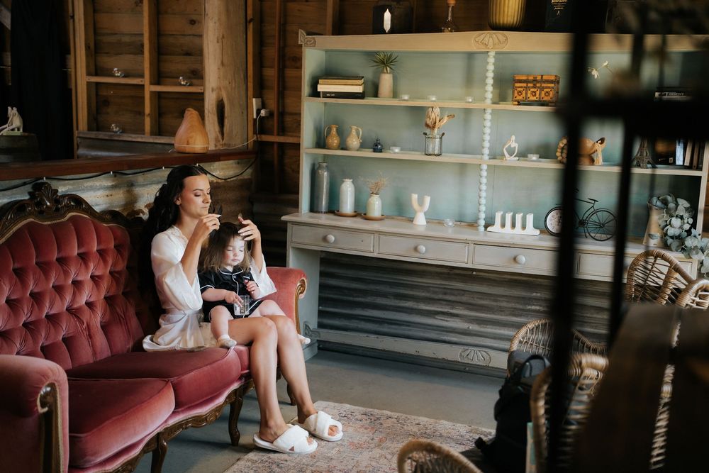 Woman sitting on a pink velvet sofa holding a child in a cozy rustic room with a blue shelving unit.