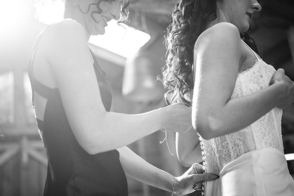 Black and white photo of a bridesmaid helping a bride with her wedding dress corset lace-up back.