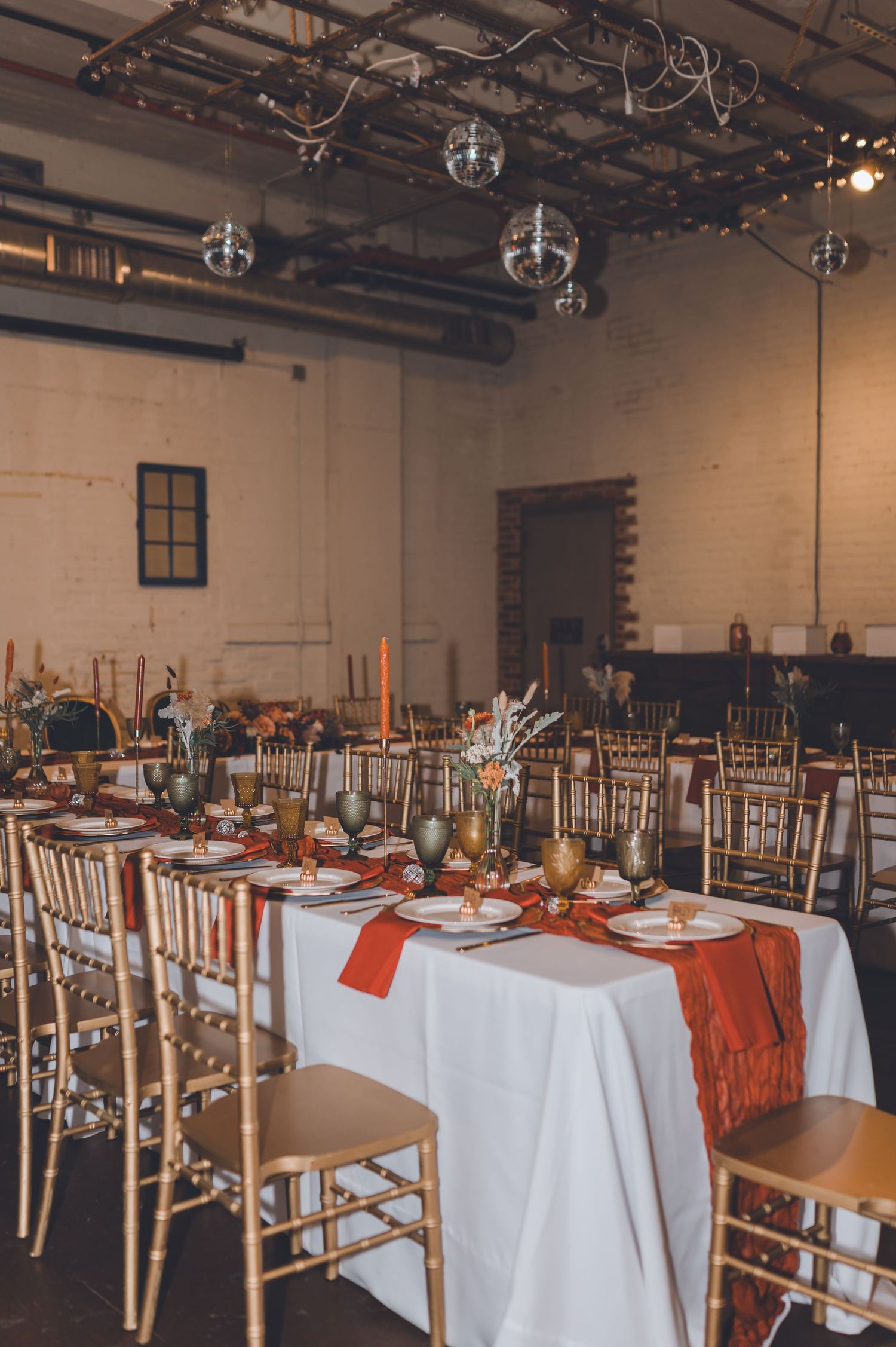 Elegant wedding reception with gold chiavari chairs, white tablecloths, orange runners, and disco ball ceiling decor.