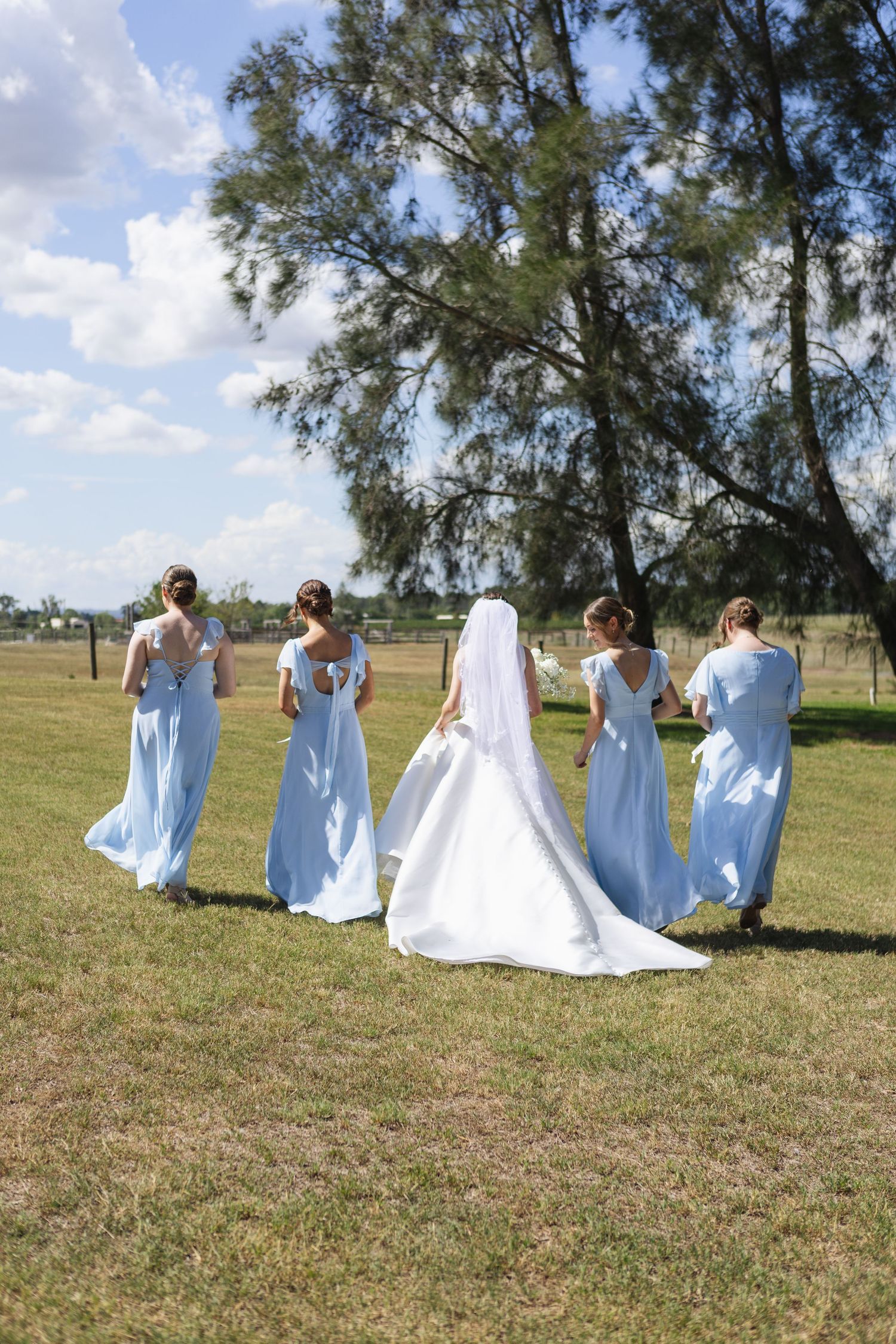 Bride and bridesmaids in blue dresses walking in field at Two Rivers Winery Wedding in Denman
