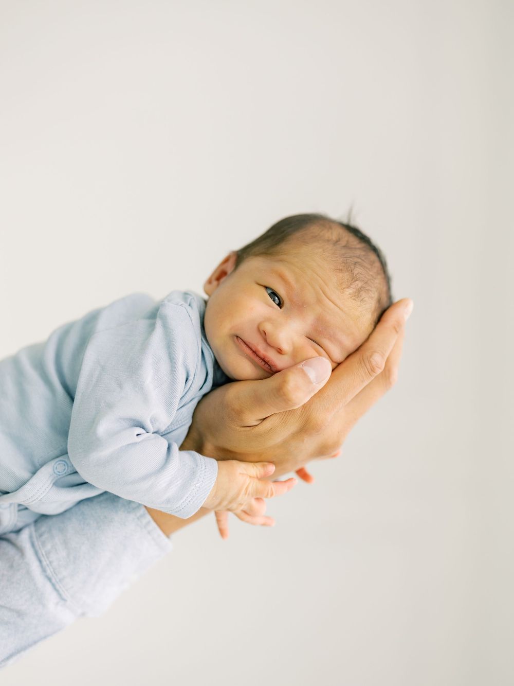 Newborn baby in light blue onesie cradled gently in adult hands against white background.