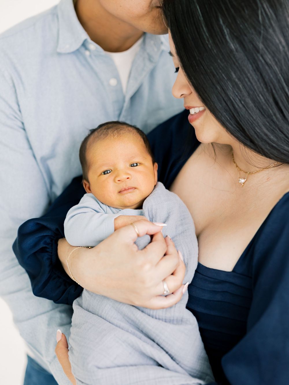 Parents lovingly holding their newborn baby wrapped in a soft blue blanket in a studio.