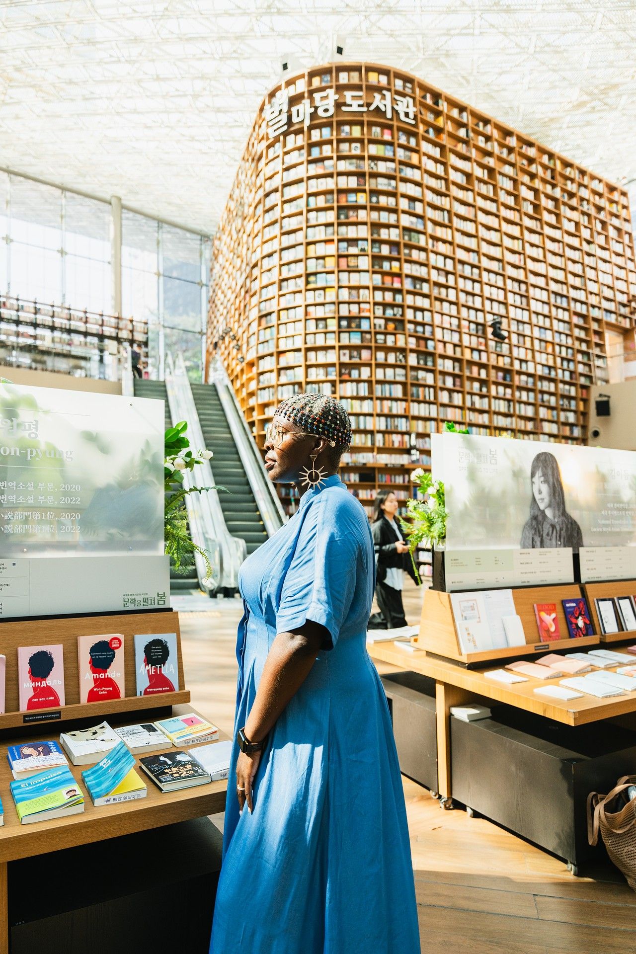 Woman in blue dress admiring a massive bookshelf wall at Starfield Library in Seoul, South Korea.