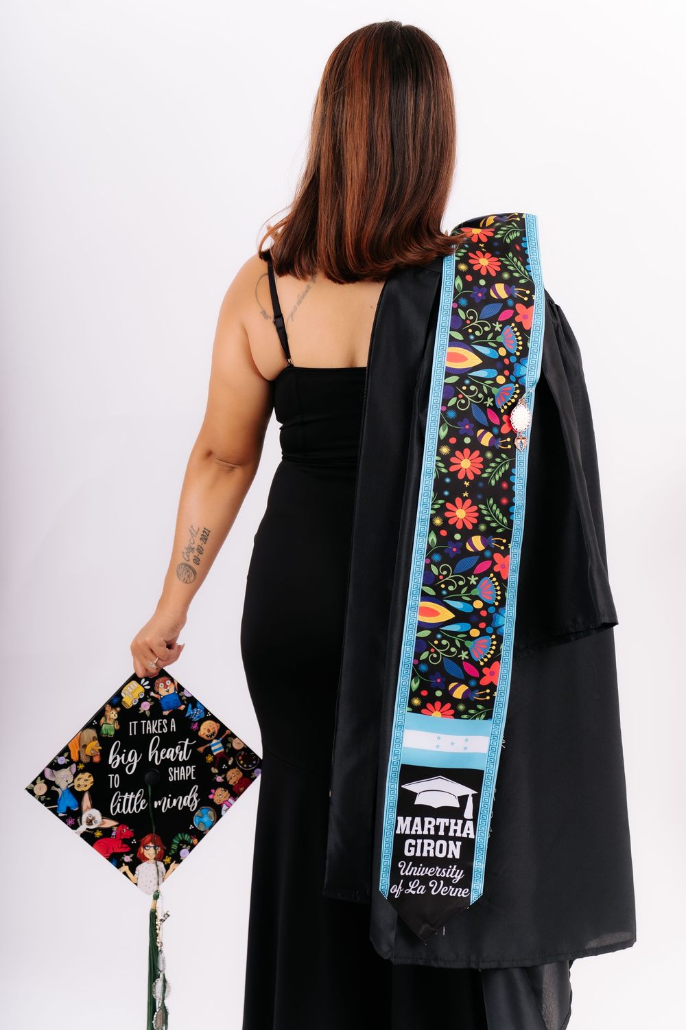 Graduate Martha Giron poses with University of La Verne cap and floral stole in black graduation gown.