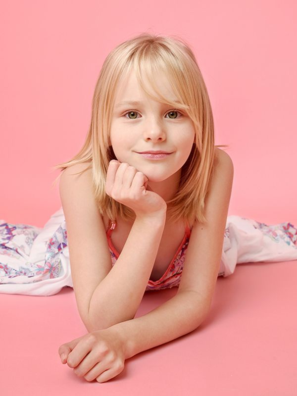 Blonde young girl with green eyes resting her head and hands on a pink background