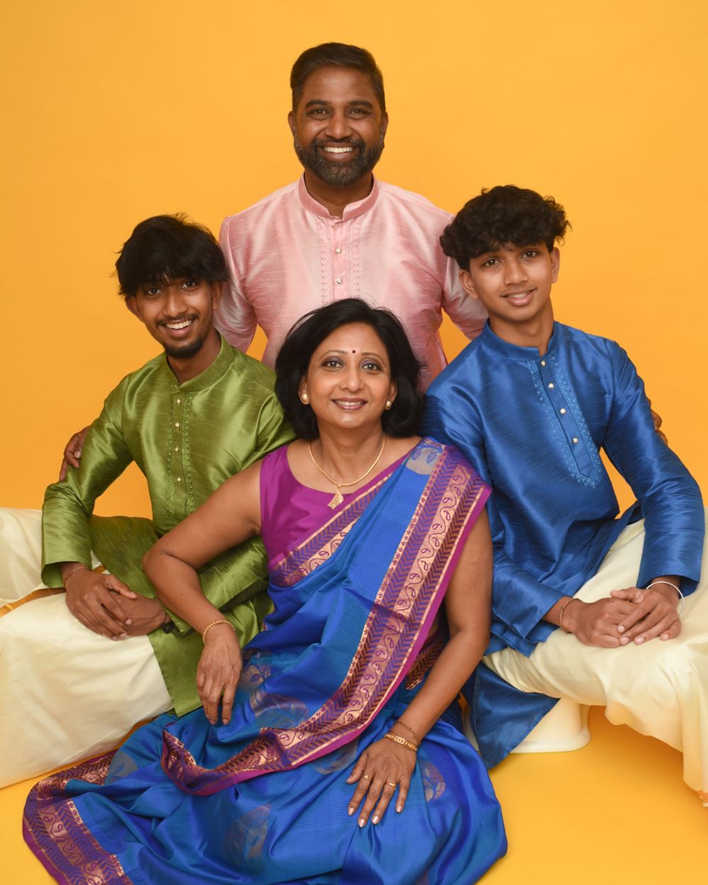 Smiling family of four posing together on a couch against a yellow background.