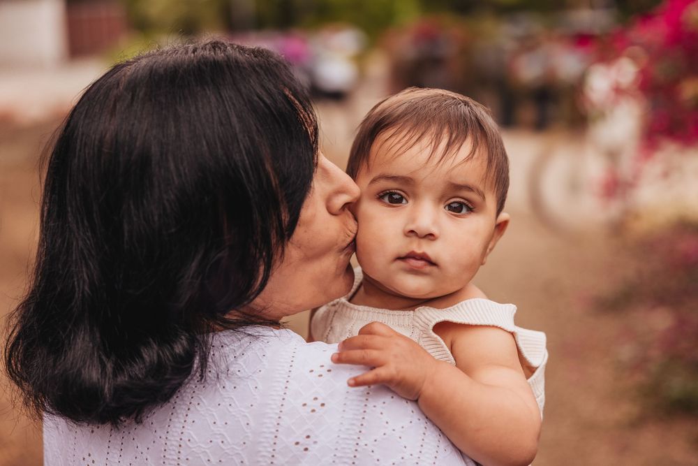 A loving mother kisses her adorable baby girl on the cheek while holding her outdoors.