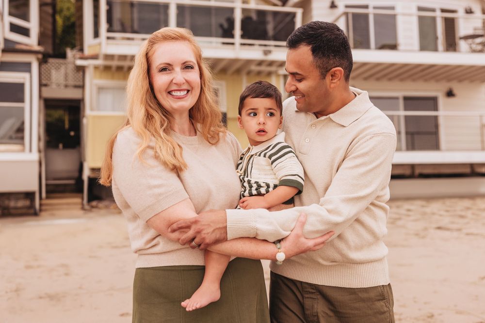 Happy interracial family smiling outdoors, parents holding toddler boy near beach house.