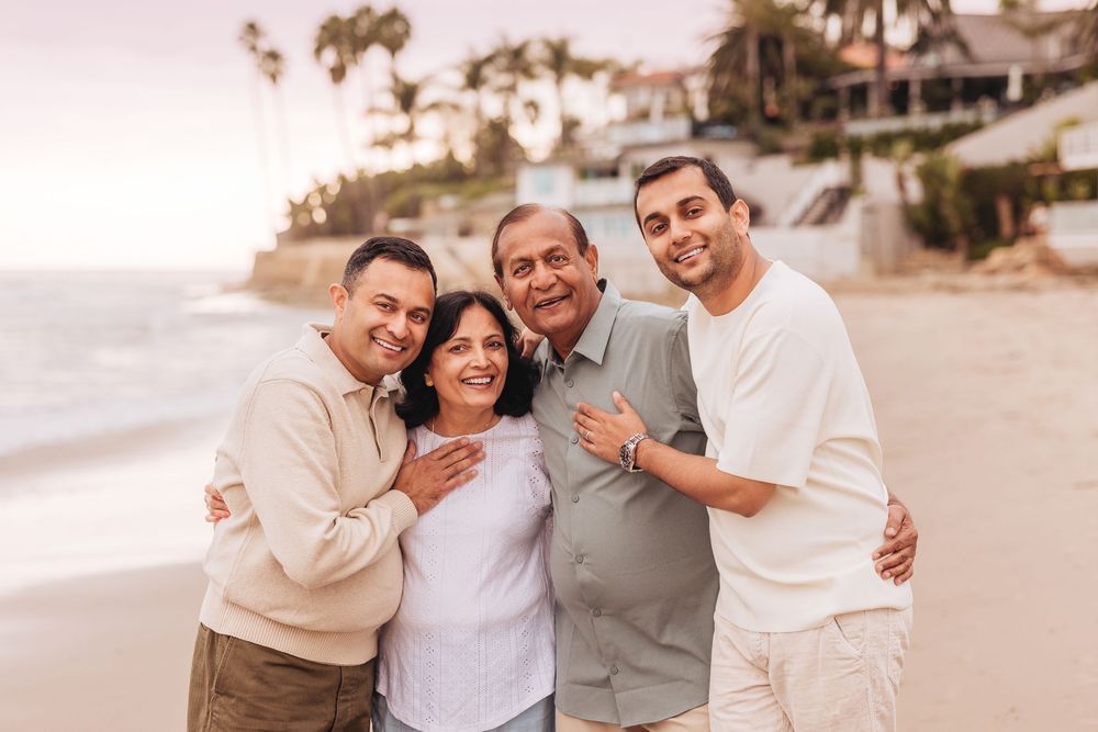 Family of four smiling together on a beach at sunset, posing for a portrait near the ocean.