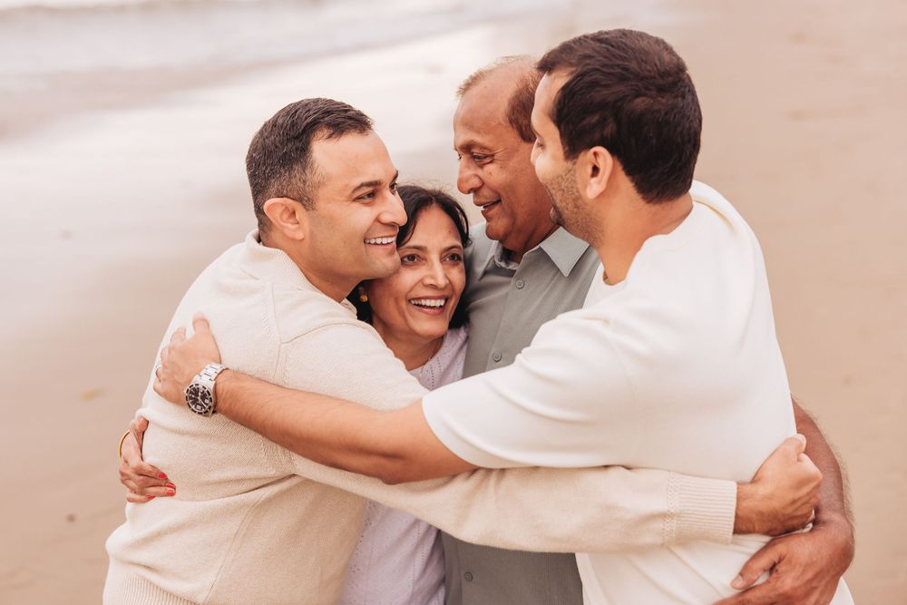 Happy family sharing a warm group hug on a sandy beach, laughing and embracing together.