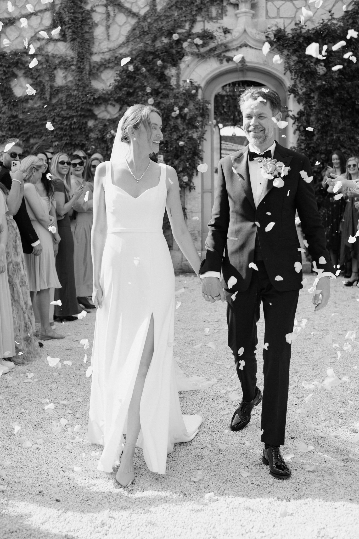 Newlyweds walking through confetti shower after outdoor wedding ceremony in black and white.