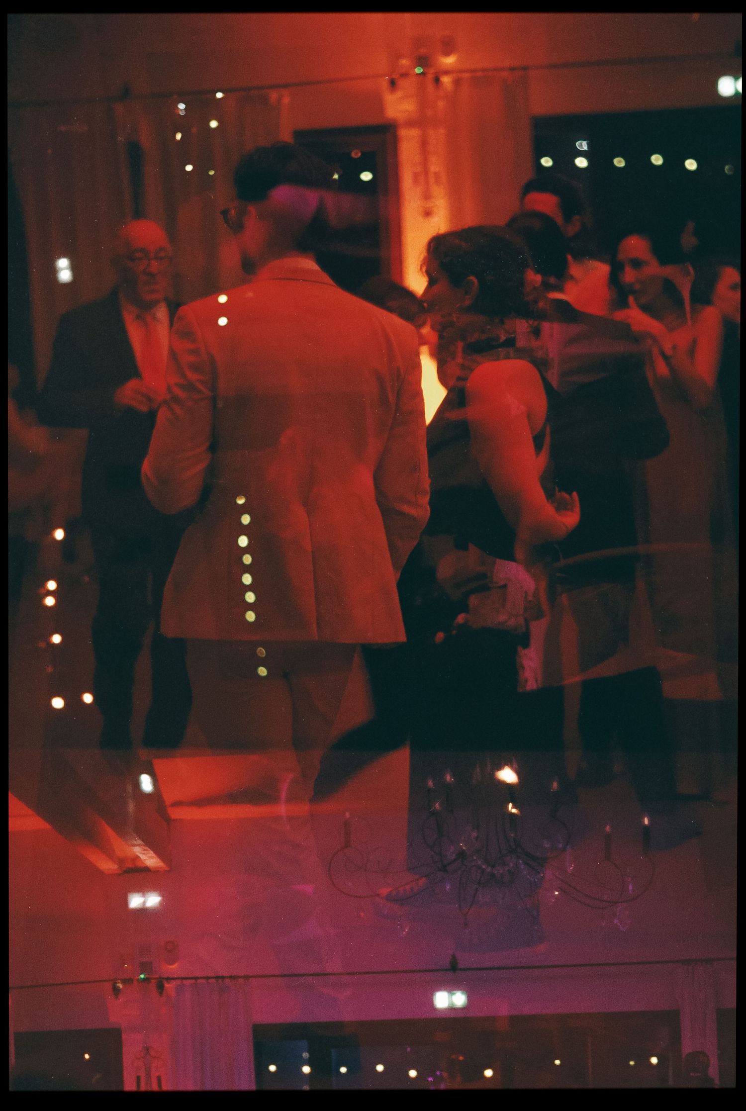 Couples dancing at a dimly lit reception venue with warm red lighting and twinkling fairy lights in background.