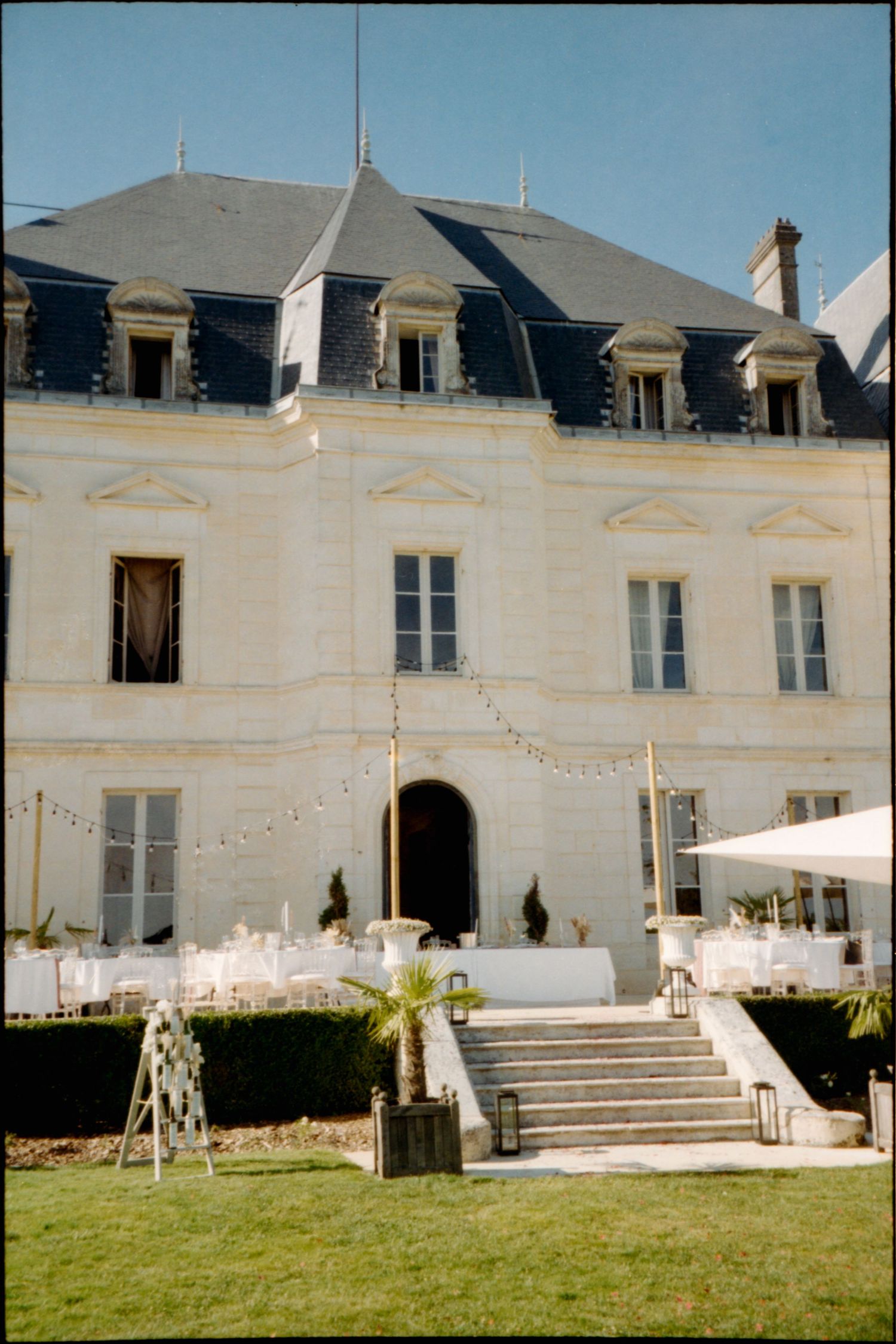 Elegant French chateau with string lights and decorative elements set up for an outdoor event on its manicured lawn.
